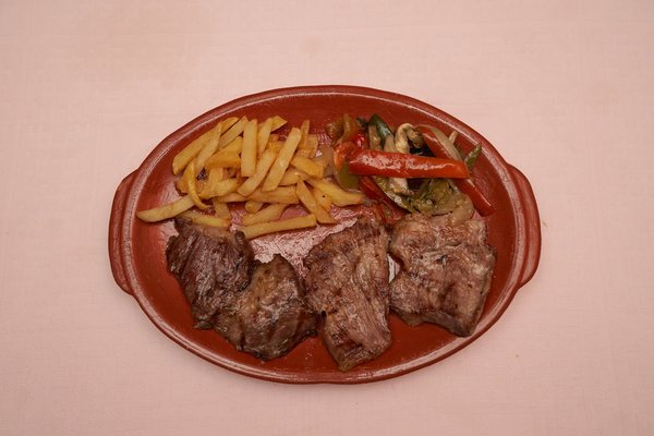 Carne a la brasa con patatas fritas y pimientos, en fuente de barro