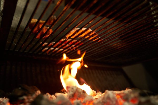Carne en la parrilla vista desde las brasas, con la llama encendida