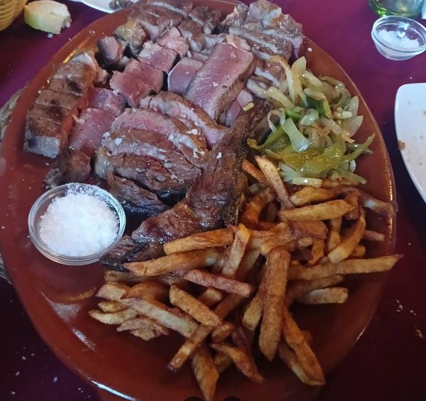 Carne de vacuno a la brasa trinchada, con patatas fritas y pimientos, servida en una fuente grande
